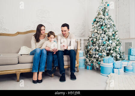 Famiglia allegra in salotto divertendosi con la tavoletta digitale che Babbo Natale ha portato la sua, dietro l'albero di Natale decorato Foto Stock