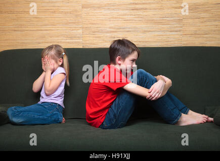 Fratello e Sorella di indossare abiti casual seduto su un divano verde back to back dopo la lotta. La ragazza si copre la faccia con le mani Foto Stock