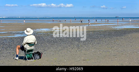 I vecchi senior citizen uomo vista posteriore in vacanza da sola seduta Ryde Isle of Wight Inghilterra UK holiday beach bassa marea viste del Solent persone paddling mare Foto Stock