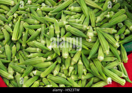 Colore verde brillante dito okra versare dal cucchiaio sul panno rosso display Foto Stock