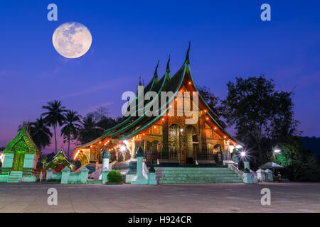 Xieng Thong tempio landmark di Luang Prabang in Laos la sera con una luna piena nel cielo. Foto Stock