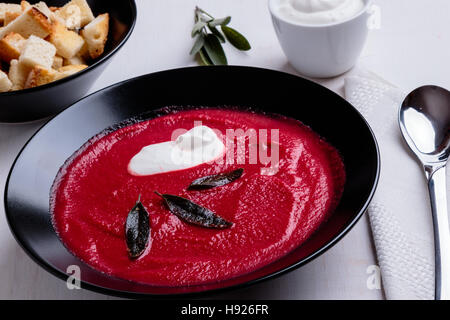 Barbabietole minestra di crema nella ciotola nero su bianco nella tabella Foto Stock