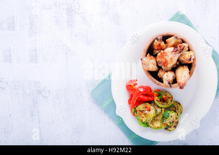 Alette di pollo fritte e zucchine, pepe su una piastra Foto Stock