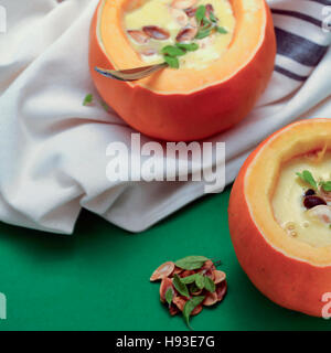 Due porzioni di zuppa di zucca in ciotole fatta di mini-zucche, su sfondo verde, guarnita con maggiorana, semi di zucca e pepe rosso, pronto per essere e Foto Stock