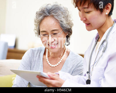 Senior donna asiatica e dal medico di famiglia avente una discussione utilizzando computer tablet Foto Stock