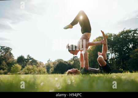 Giovane uomo e donna fare yoga in coppia all'esterno. Giovane facendo acro yoga nel parco. Foto Stock