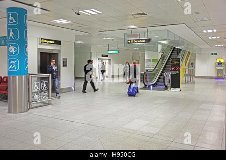 Interno di Gatwick Airport North terminale mostra di ascensori e scale mobili seguendo le indicazioni per "epartures' con una gamma di altri segni Foto Stock