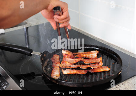 African American uomo pancetta di cottura sul fornello con una padella per grigliare Foto Stock