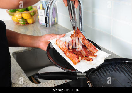 African American uomo pancetta di cottura sul fornello con una padella per grigliare Foto Stock