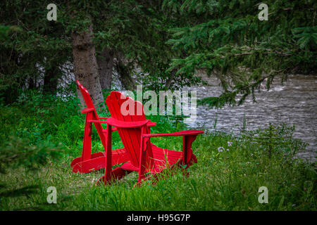 Due rossi sedie Adirondack seduta da un fiume. Foto Stock