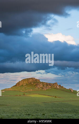 Vista della collina di Almscliffe Crag illuminata dal sole (gritstone tor, campi verdi separati da pareti di pietra, splendido paesaggio collinare) - North Yorkshire, Inghilterra UK. Foto Stock