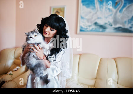 Giovane bella bruna medicazione sposa abito di seta e tenere grandi gatto grigio sulle mani Foto Stock