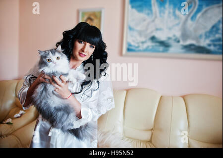 Giovane bella bruna medicazione sposa abito di seta e tenere grandi gatto grigio sulle mani Foto Stock