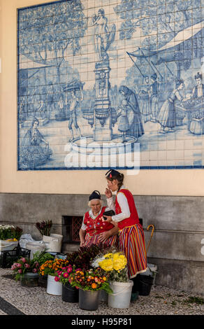 Venditori di fiori nel tradizionale costume di Madeira al mercato di Funchal con colorati fiori tropicali di fronte blu del pannello di piastrelle Foto Stock