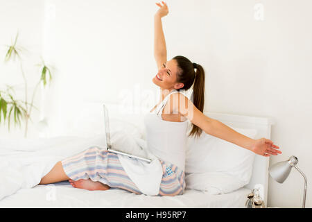 Giovane donna stretching nel letto mentre il suo lap top in piedi sulle gambe Foto Stock