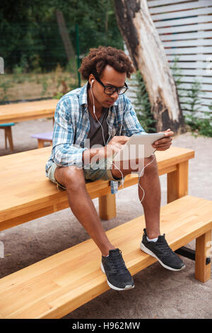 Concentrato di giovani africani uomo utilizzando auricolari e tablet in patk Foto Stock