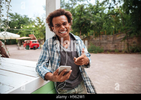 Allegro african giovane uomo ascoltare musica dal telefono cellulare e ridere Foto Stock