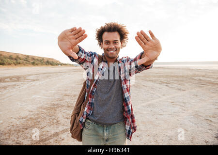 Allegro uomo africano con zaino focalizzazione tramite le sue mani sulla spiaggia Foto Stock