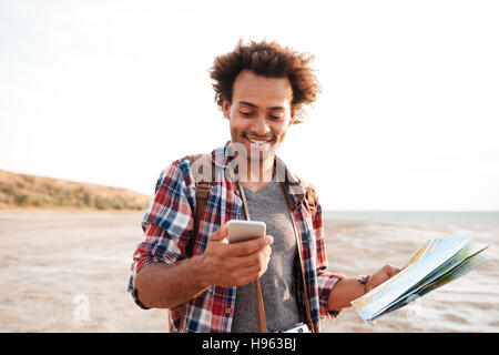 Sorridente americano africano giovane uomo usando la mappa e il telefono cellulare all'aperto Foto Stock