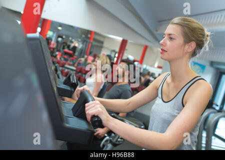 Montare la bionda utilizzando la fase macchina in palestra Foto Stock