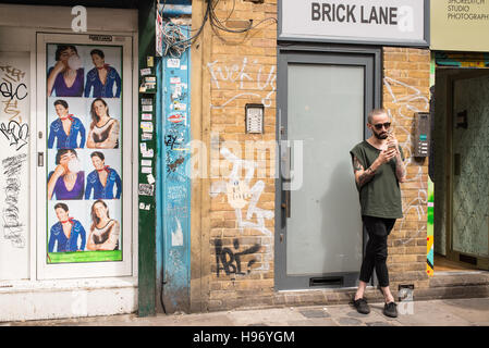 Hipster uomo con bracci tatuati di fumare una sigaretta in Brick Lane, Shoreditch, Londra, Regno Unito. Foto Stock