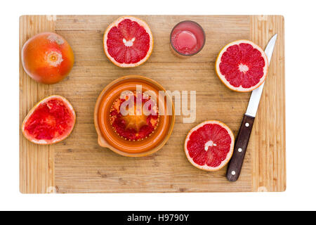 Angolo alto ancora la vita di fettine di rosso rubino pompelmo agrumi con centrifuga e coltello affilato sul tagliere di legno Foto Stock