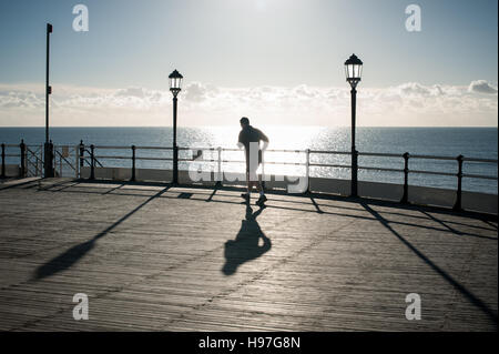 Un uomo che corre lungo Worthing Pier si stagliano contro il mattino luminoso sole autunnale a Worthing, West Sussex, Regno Unito. Foto Stock