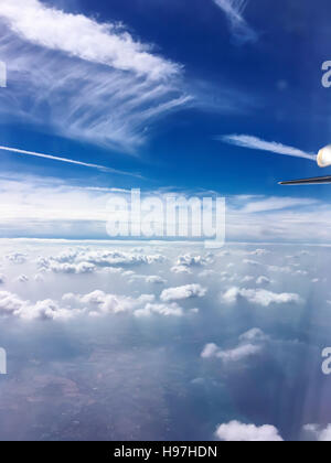 Volo sopra white cumulus nubi in un aereo con il wingtip e sentiero di vapori visibili in una soleggiata cielo blu in un concetto di trasporto Foto Stock