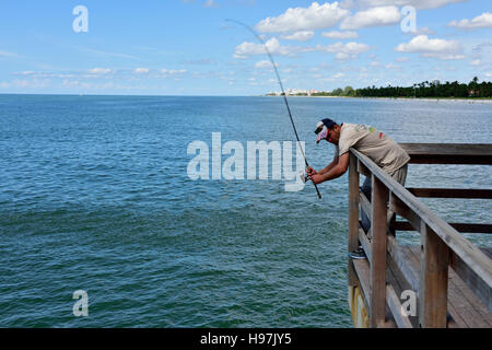 Pescatore solitario con asta e vero e proprio poggiando sul corrimano fuori Napoli molo, Florida, Stati Uniti d'America Foto Stock