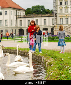 I bambini guardano a cigni in uno stagno esterno Nymphemburg Palace a Monaco di Baviera, Germania Foto Stock