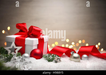 Scena di Natale con una scatola regalo bianca, arco rosso e nastro, luci, baubles, Abete rami e neve, con spazio di copia Foto Stock