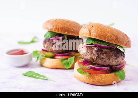 Grande panino - hamburger burger con carne di manzo, sottaceti, pomodoro e cipolla rossa su uno sfondo luminoso. Foto Stock