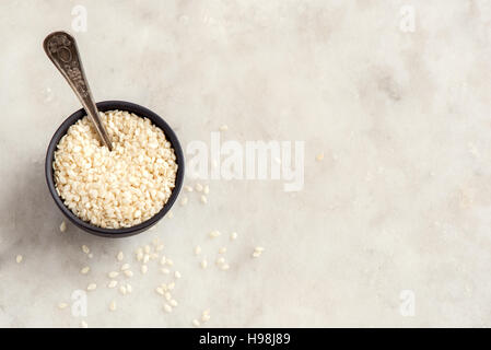 I semi di sesamo in coppa sopra pietra bianca con sfondo spazio copia - il cibo sano ingrediente Foto Stock