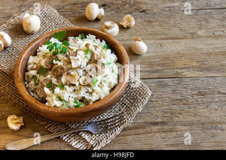 Risotto ai funghi con il prezzemolo nel recipiente di legno su sfondo rustico con copia spazio - una sana alimentazione vegetariana Foto Stock