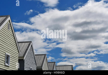 Andando verso nord nel paesaggio nordici: una fila di case costruite in tipica architettura in legno, cielo blu e nuvole Foto Stock