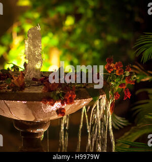 Una fontana decorata con fiori rosa che gorgoglia di notte sulla terrazza sul tetto del Riad Arabesque a Fès, in Marocco, con l'acqua che gocciola dal bordo della vasca. Foto Stock
