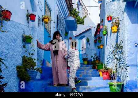 Un giovane ragazzo aiuta una signora anziana giù alcuni passi in una strada nella Medina, Chefchaouen, Marocco Foto Stock