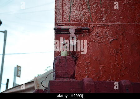 Close-up di un lucchetto rosso con meccanismo di bloccaggio su un dipinto di rosso porta in ferro con sfondo sfocato Foto Stock