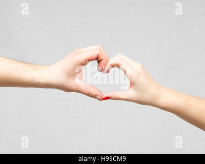 Maschio e femmina rendendo le mani a forma di cuore su uno sfondo grigio. Foto Stock