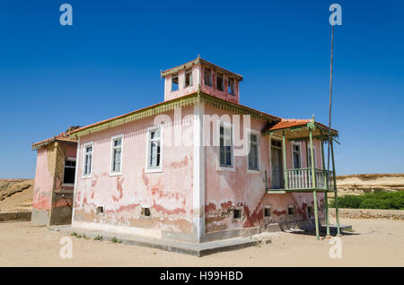 Grande rosa rovinato mansion dal portoghese di epoca coloniale nel piccolo villaggio costiero di Angola il deserto del Namib. Foto Stock