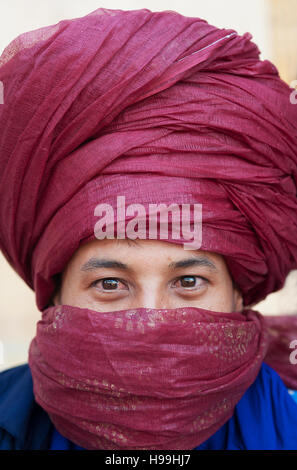 Ritratto di un nomade beduino con turbante rosso scarlatto e fissando gli occhi vende la sua mercanzia in Ait Benhaddou, Marocco. Foto Stock