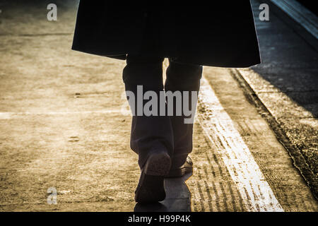 Un pendolarista che indossa un trench che cammina lungo il bordo della piattaforma a Londra, Regno Unito Foto Stock