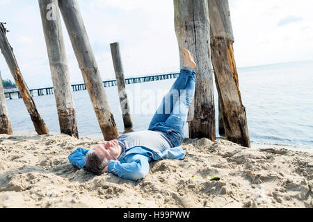 Uomo che stabilisce sulla spiaggia con i piedi fino Foto Stock