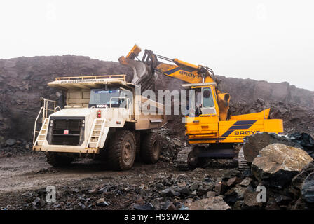 Un Broyt caricatore cingolato carichi fino a Terex rock dumper in una cava in heavy rain. Foto Stock