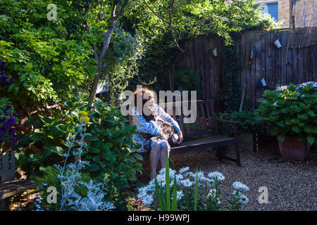 Le donne in vestaglia seduti in giardino sul banco di lavoro con un cane Foto Stock