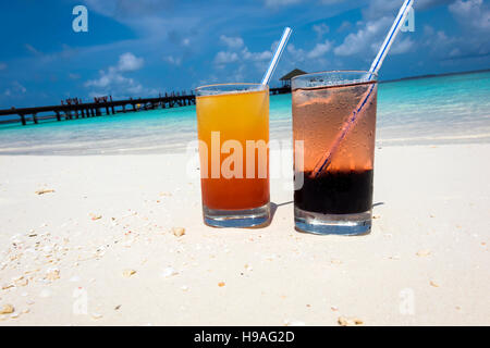 Due cocktail colorati recante sulla sabbia bianca, piccoli coralli spiaggia coperta di fronte all'incredibile acqua turchese dell'indiano oc Foto Stock