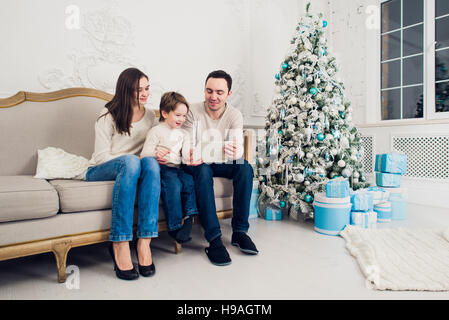 Famiglia allegra in salotto divertendosi con la tavoletta digitale che Babbo Natale ha portato la sua, dietro l'albero di Natale decorato Foto Stock