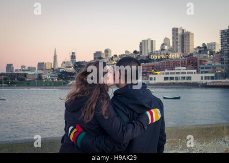 Una giovane coppia in amore al Parco Acquatico del molo, con il Parco Acquatico Bathhouse, Ghirardelli Square e la skyline di San Francisco. Foto Stock