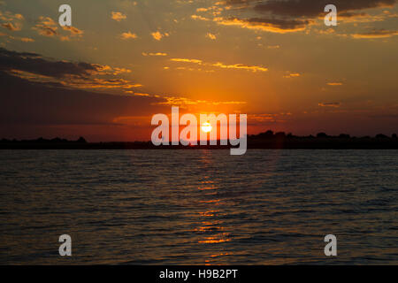 Tramonto africano con crimson sky come il sole è in procinto di affondare sopra il fiume Chobe Foto Stock