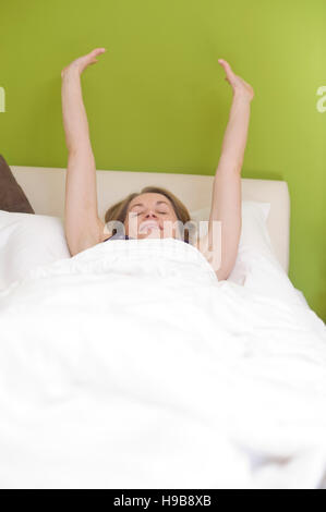 Giovane donna nel letto, allungando le braccia dopo il risveglio Foto Stock